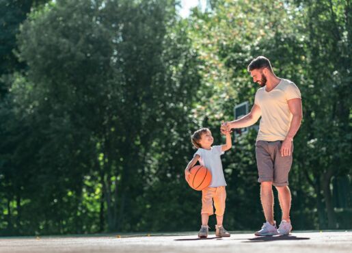 Kind mit Ball in der Hand mit Vater vor Basketballplatz